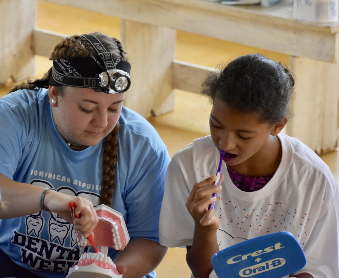 dental hygiene student shows child how to brush teeth