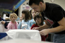 Children watch a Penn College student screen-print a design onto their T-shirts