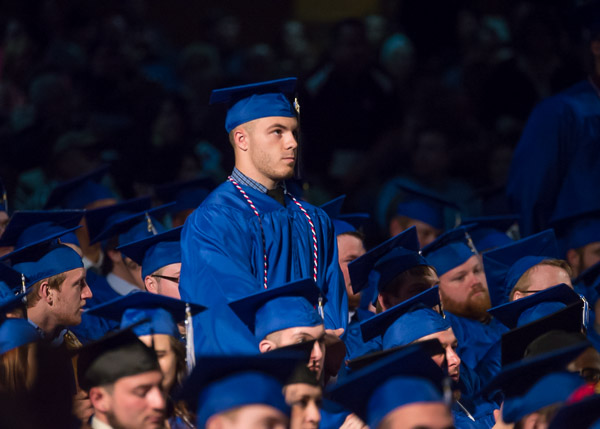 A patriotic honor cord adorns a veteran, who, in a scene repeated in all three of the weekend's ceremonies, stands among his classmates to appreciative applause from the audience.