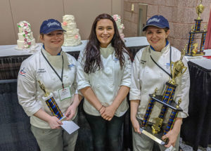 Penn College students took first- and third-place awards in the Student Tiered Wedding Cake category at the 2018 Atlantic Bakery Expo. Three Penn College students competed. From left are Taylor M. Bickhart, of Middleburg, who received third place; Sarah A. Waclo, of York; and Jacqueline R. Dull, of Mohnton, who took first place. Their respective cakes are behind them.