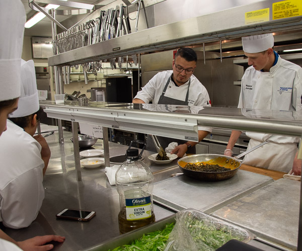 Students gather around Uribe, who demonstrates the final preparation and plating for a pasta dish. At right is student Hunter K. Jordan, of Middleburg.