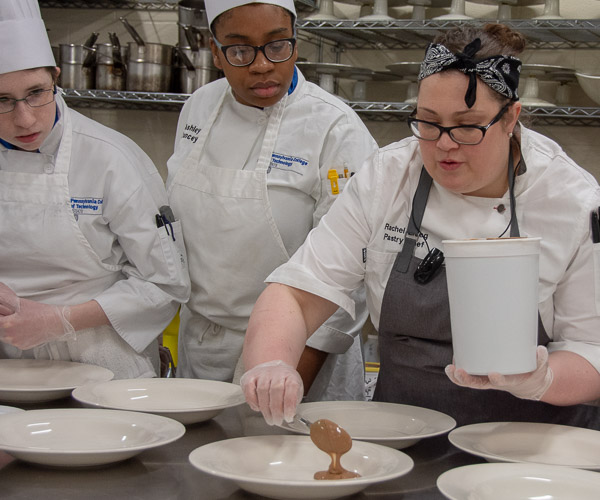 Danielle R. Wesneski (left), of Williamsport, and Ashley L. Yancey, of Abington, watch closely as Erceg demonstrates how to plate the dessert.