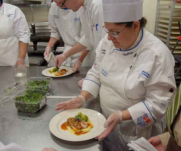 Chef Mary G. Trometter, assistant professor of hospitality management/culinary arts, passes a finished plate to a server.