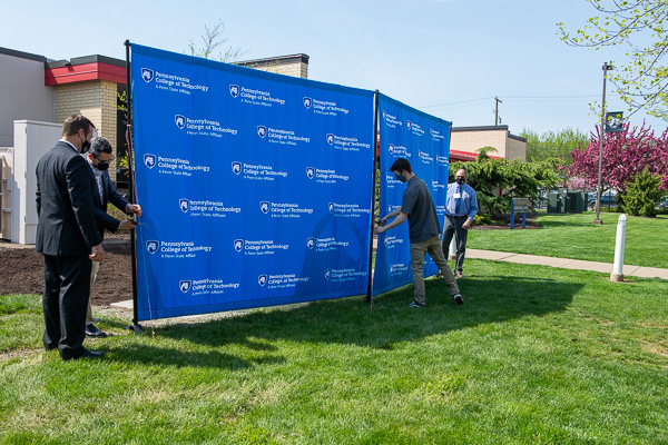 Those assigned roles in the suspenseful reveal move into place, preparing to pull away the display banners. From left are Andy Yencha, operations manager at Pacproinc; Capps; Harrison; and Howard W. Troup, instructor of automated manufacturing/machine tool technology.