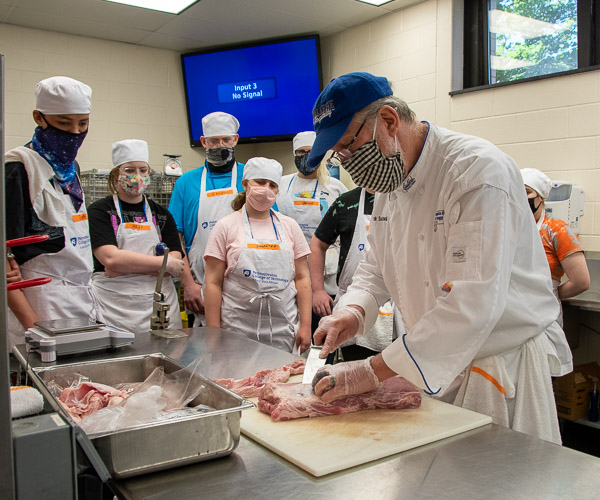 Chef Frank M Suchwala, associate professor of hospitality management/culinary arts, demonstrates how to trim a pork tenderloin during Future Restaurateurs. Suchwala oversaw the savory portion of the five-day program that culminated in a participant-produced Asian fusion dinner for the teens’ families. Chef Charles R. Niedermyer, instructor of baking and pastry arts and culinary arts, supervised baking and pastry production.