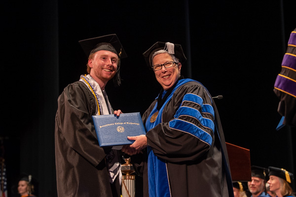 Gilmour and nursing grad Connor J. Burke, a member of the Wildcat baseball team, enjoy their on-stage meeting. Burke was presented with a commencement award that memorializes Linda F. Clark, a former director of nursing at the college.