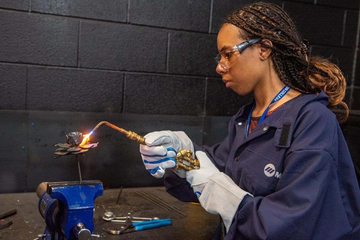 Blossoming in the welding lab, a “Tinker-Belle” concentrates on heat-forming her metal rose.
