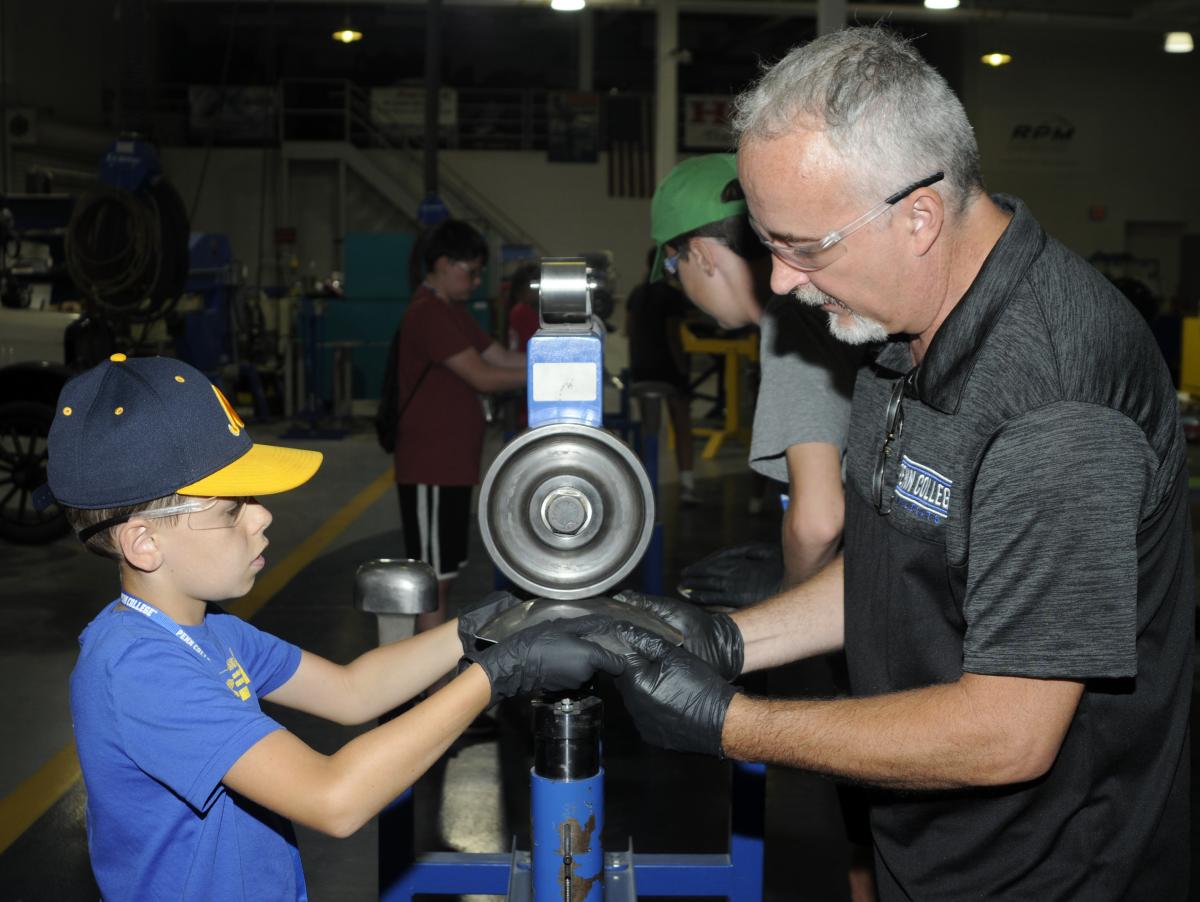 The experienced (and helping) hands of Roy H. Klinger, collision repair instructor, lend confidence to a boy shaping metal on the English wheel.