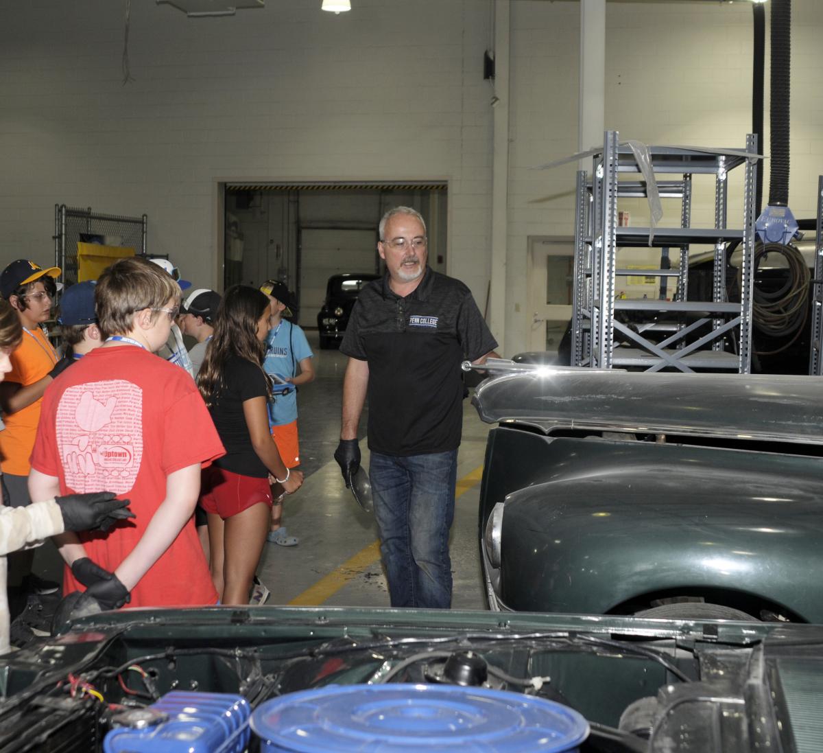 The instructor leads a brisk and informative walk-through among the vintage automobiles entrusted to Penn College restoration students by museums and other collectors.