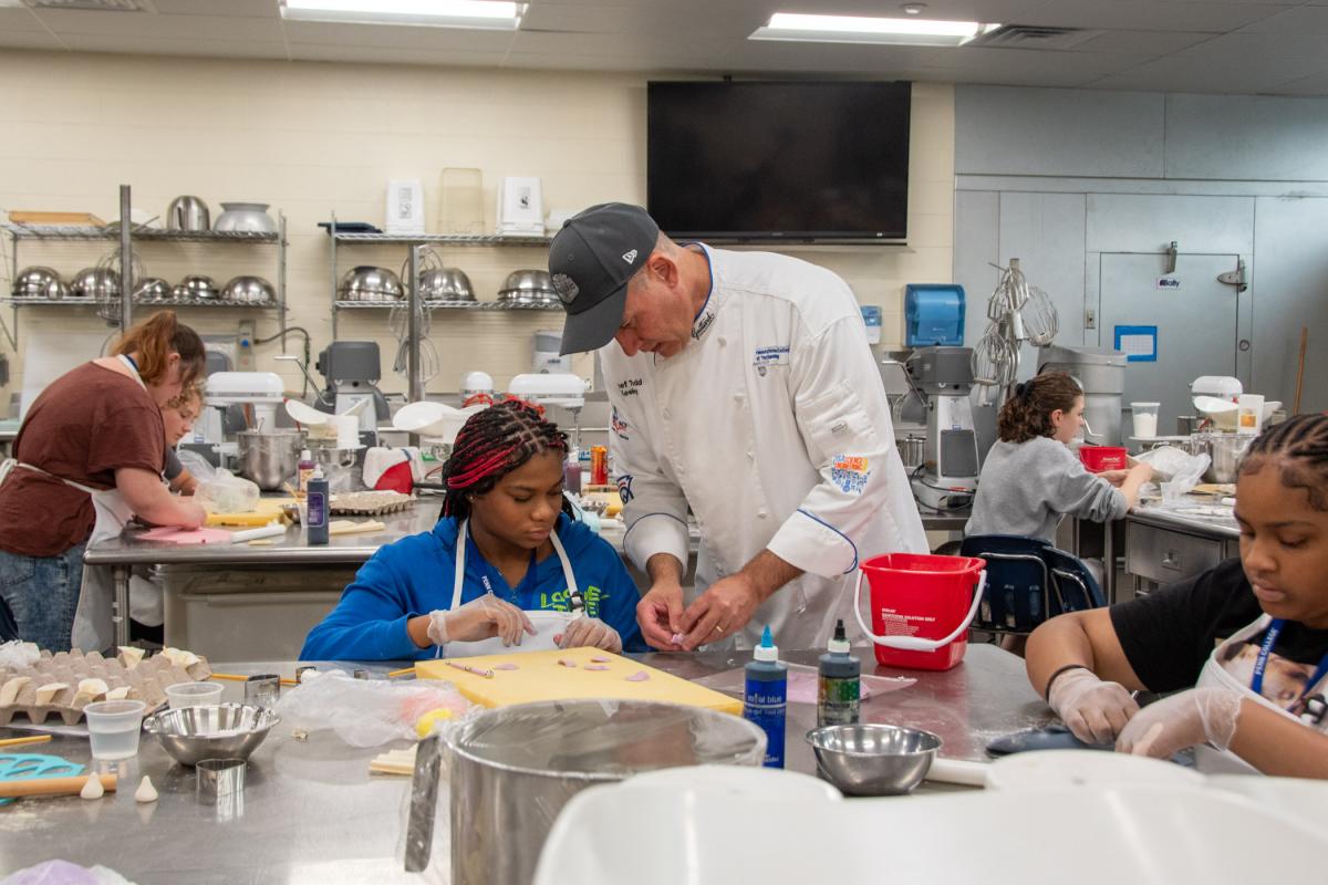 Chef Todd M. Keeley, assistant professor of baking and pastry/culinary, lends his know-how for forming roses from gum paste. The Have Your Cake and Decorate It, Too, program represented the first time any of the participants had worked with the medium. They used it to form calla lilies, roses and bows.