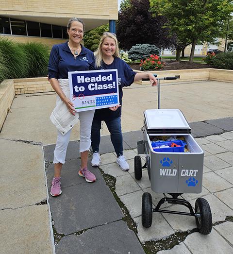 Wheeling a "Wellness Cart" full of goodies, complete with a bicycle bell, are Mary Shuma Rudberg (left) director of counseling; and Wendie L. Snyder, director of college health services.