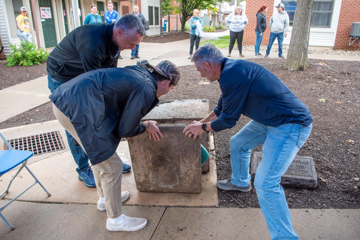 Assisted by President Reed and Resident Assistant Aidan J. Weissenberger, Mallery moves the time capsule’s heavy lid for removal of the once-buried treasures.