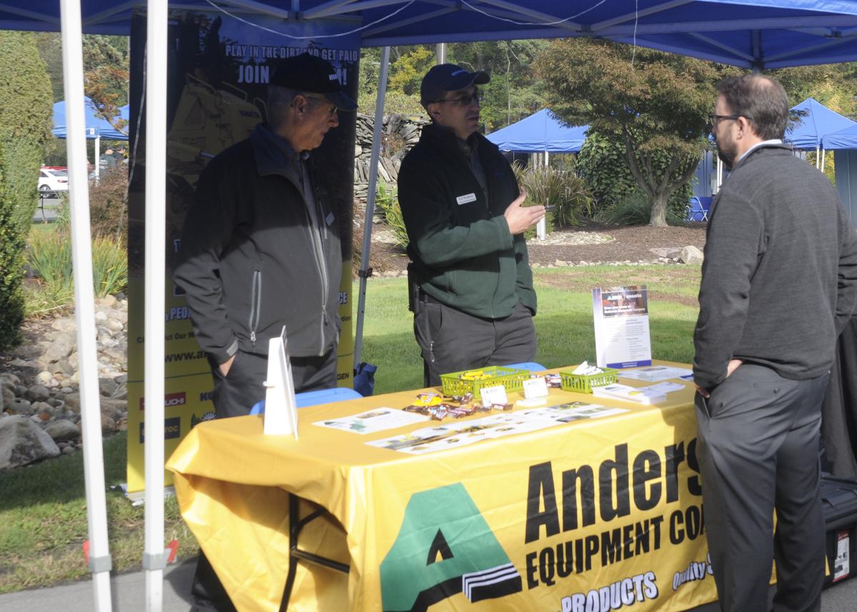 Though partially obscured by the shade of their tent, representatives of Anderson Equipment Co. bring opportunity to light. Talking with Justin W. Beishline, assistant dean of diesel technology and natural resources, are Ed Wallace (left), academic recruiting manager, and Jerry Skiff, director of service. Both were also on hand in March, accompanied by an excavator on loan for student instruction.