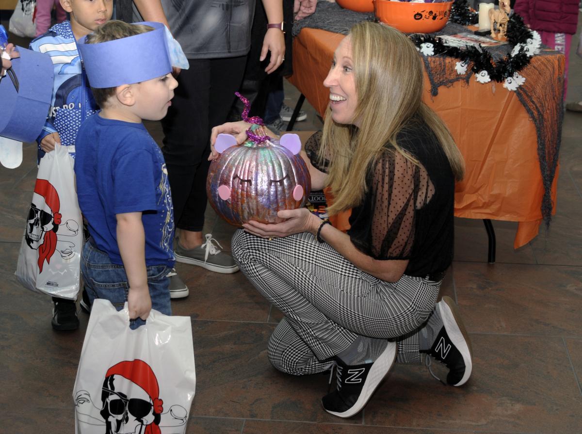 Hillary E. Hofstrom, vice president for people and culture, gets down to a child's level for eye-to-eye bonding over a shimmery pumpkin.