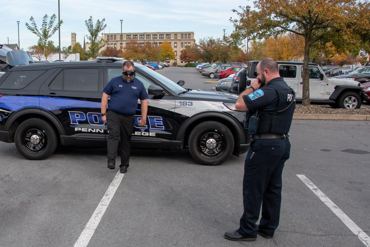 Wearing goggles that simulate the effects of an over-the-legal-limit blood alcohol content, Timothy O. Rissel, executive director of general services, follows the instruction of Officer Jeffrey L. Hughes to attempt the one-leg stand sobriety test.