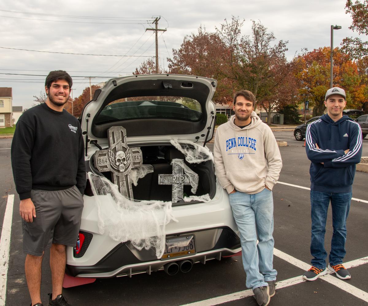 Penn College Motorsports Association members and automotive technology students Sal Leuzzi, of Mount Laurel, N.J. (left, also pursuing automotive technology management), and Alexander S. Broyles (center), of Chadds Ford, offer graveside treats. They are joined by Cameron I. Myers, of Hollidaysburg, automotive technology, who stopped by the event.