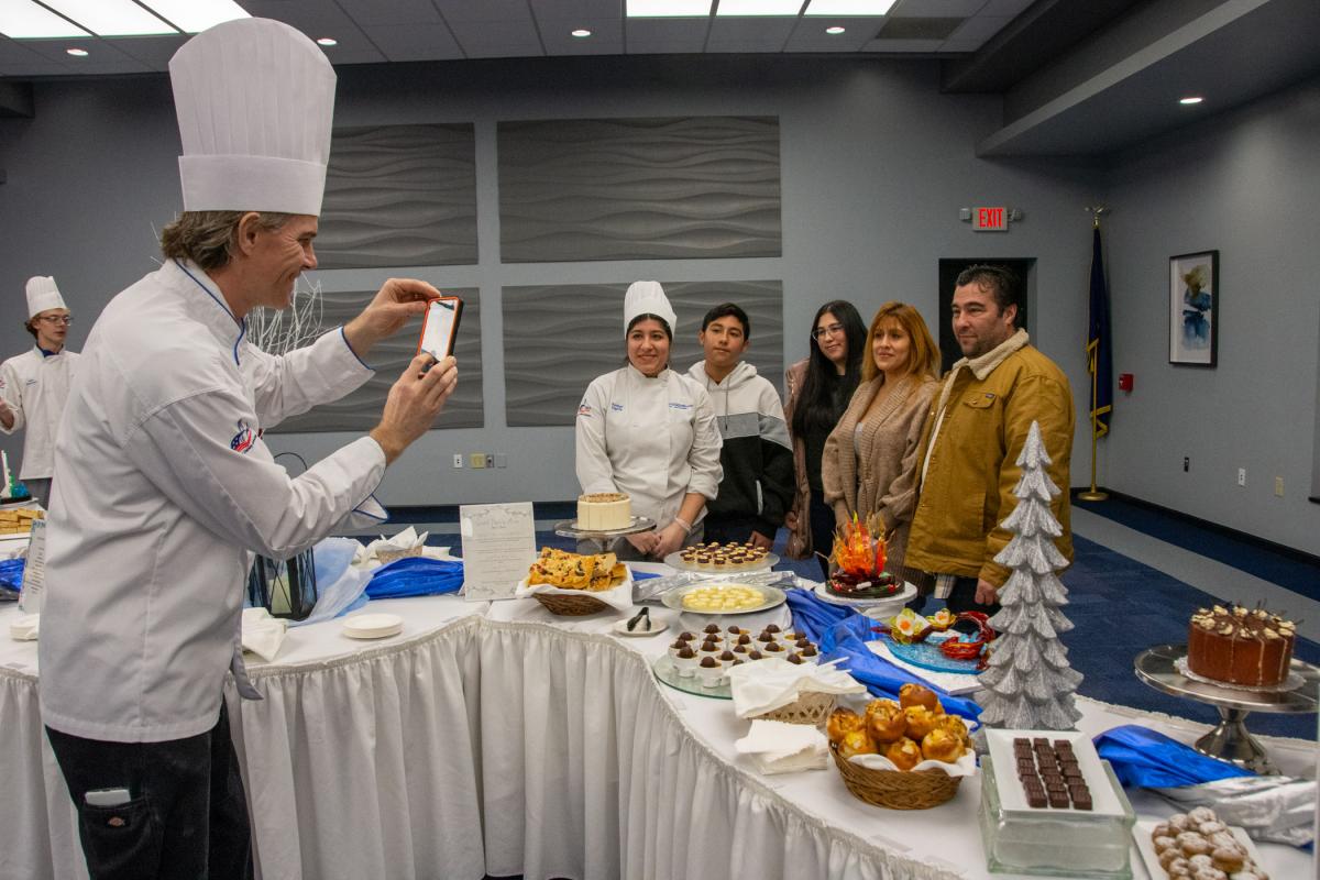 Chef Charles R. Niedermyer, instructor of baking and pastry arts/culinary arts, takes a photo of Amber R. Harris, of Sciota, and family, with her capstone display.