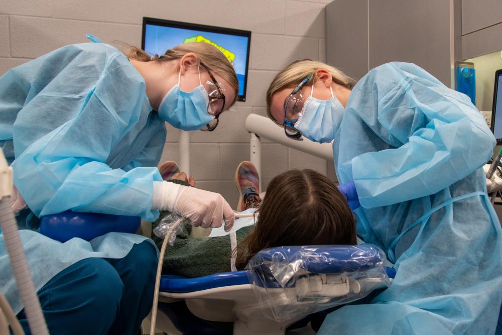 two dental hygiene students working on a patient