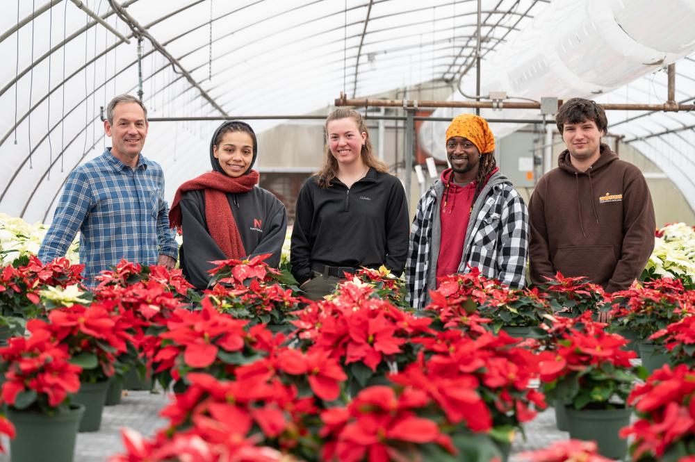 group photo of PLNA rep and four student scholarship recipients in a poinsettia-filled greenhouse