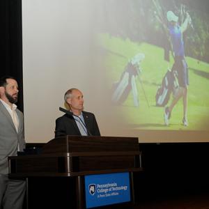 Sharing emcee duties, Blymier and Kennell await the start of the ceremony beneath a projected photo from a Penn College golf match. Earlier in the weekend, the Wildcat golf team won its second conference championship in three years.