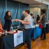 Markell Kunigus, customer service executive for The Hartman Group, offers a welcoming handshake while, in the background, students interact with Bayard Printing Group and Jersey Shore State Bank. Kunigus is joined by Ashley Sitler, a Hartman customer service representative.