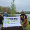 Students hold the Tree Campus Higher Education banner in front of a newly planted weeping willow.