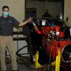 Michael J. Sormilic, an online power generation student from Southbury, Conn., who has spent much of the Fall 2020 semester learning the ins and outs of the equipment, stands alongside a Cummins crane engine donated to Penn College by Terex Corp. Behind him, in the control room of the dyno lab, are John D. Motto (left), diesel equipment technology instructor, and Chris Macdonald, assistant director of corporate relations.